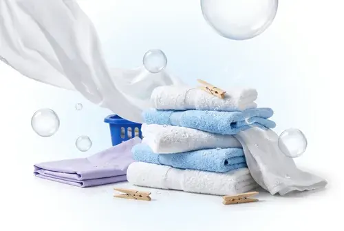 Toalhas e um lençol dobrados em tons de azul e lilás, com prendedores de roupa de madeira e bolhas de sabão